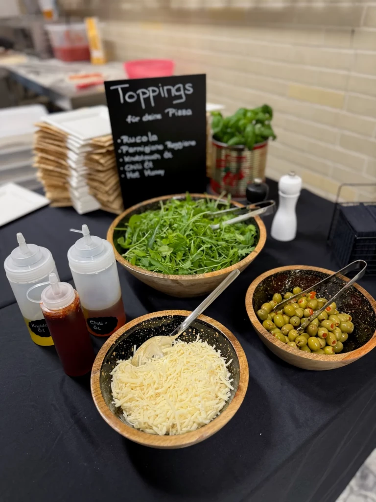 Pizza-Toppings zum Selbstbelegen: frischer Rucola, geriebener Parmesan und Oliven