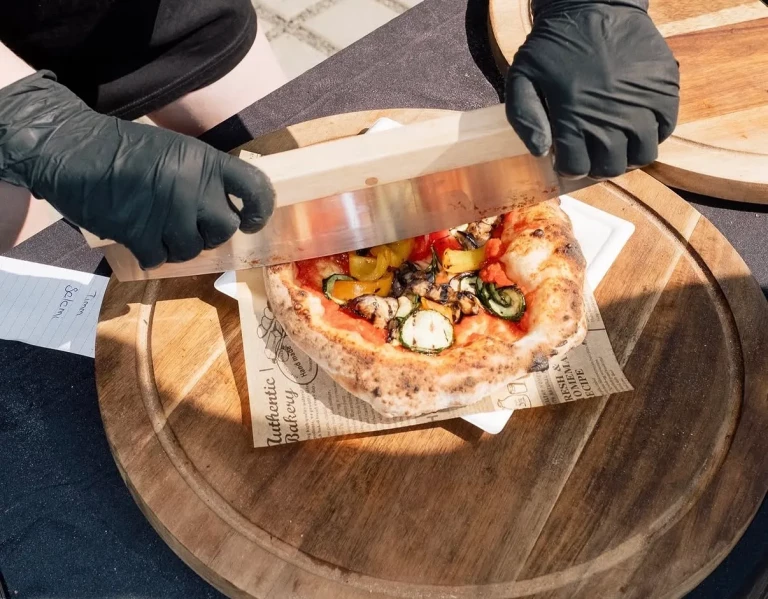 Pizza Verdura mit gegrilltem Gemüse wird mit dem Pizzaschneider geschnitten