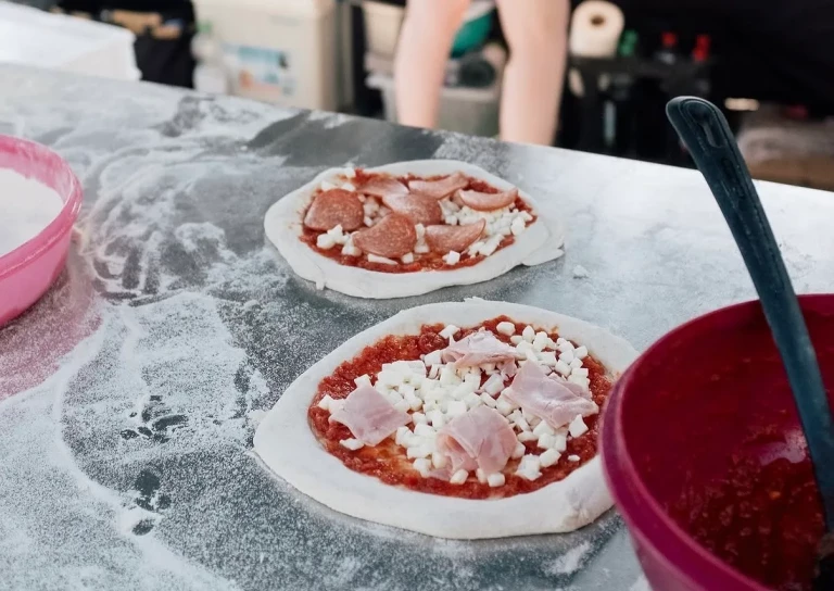 Belegte Pizzateiglinge mit Salami, Schinken und Fior di Latte auf dem bemehlten Arbeitstisch