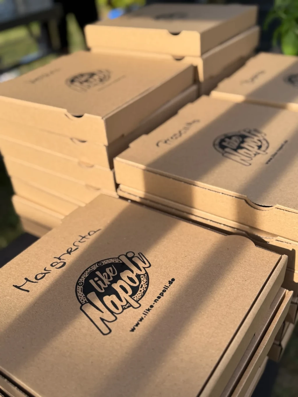Gestapelte Like-Napoli-Pizzakartons mit handbeschrifteten Sorten in der Spätsommersonne