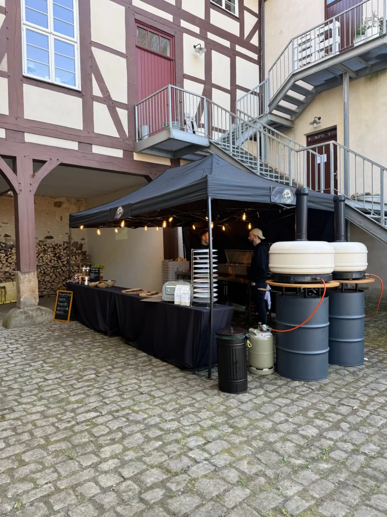 Pizzastand mit zwei mobilen Pizzaöfen unter schwarzem Pavillon im Fachwerk-Innenhof des Ritterguts Goltern