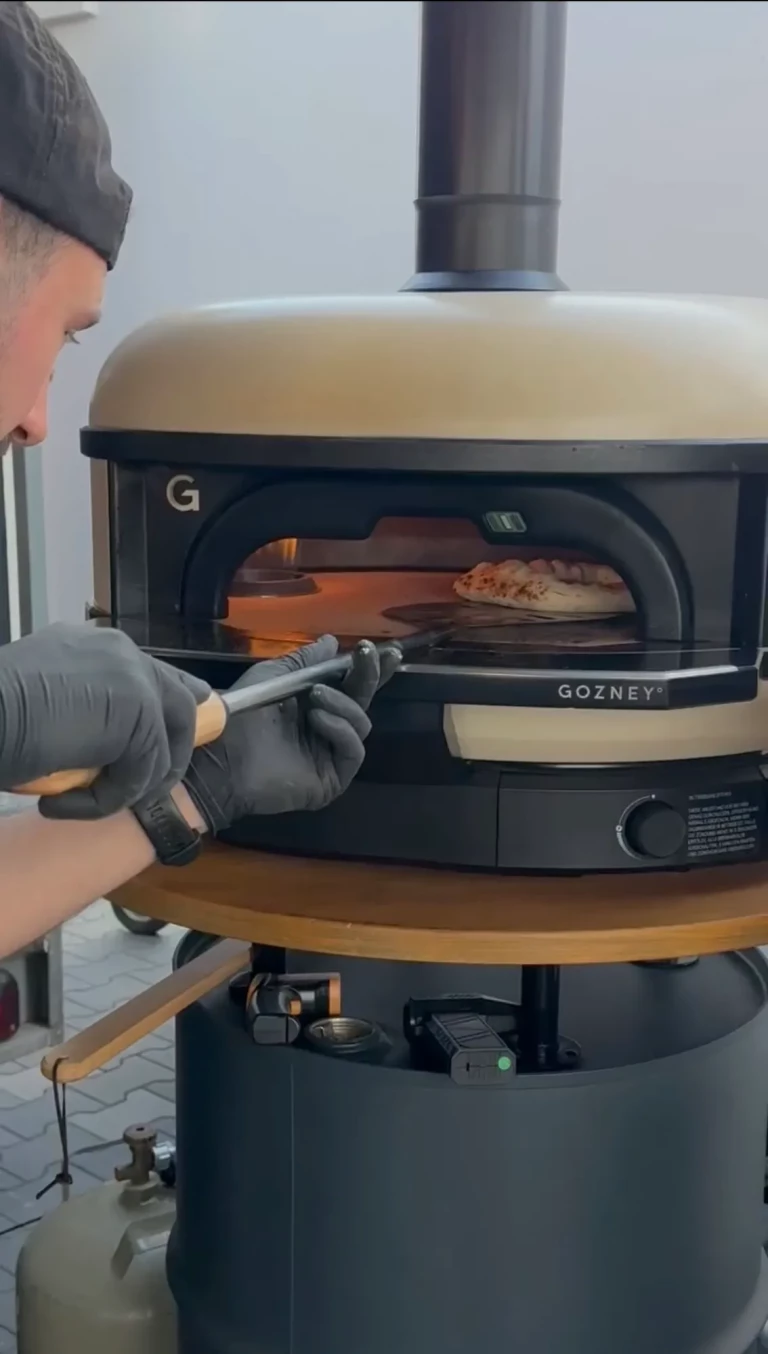 Pizzabäcker wendet eine Pizza im mobilen Gozney-Pizzaofen