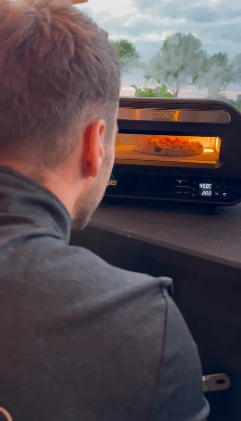 Blick über die Schulter des Pizzabäckers auf den Ofen, in dem eine Pizza backt