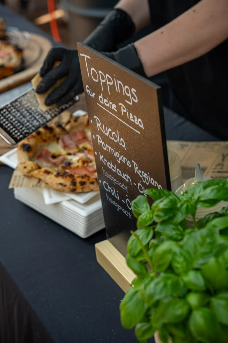 Toppings-Tafel mit Rucola, Parmigiano Reggiano und Chili-Öl, davor frisches Basilikum